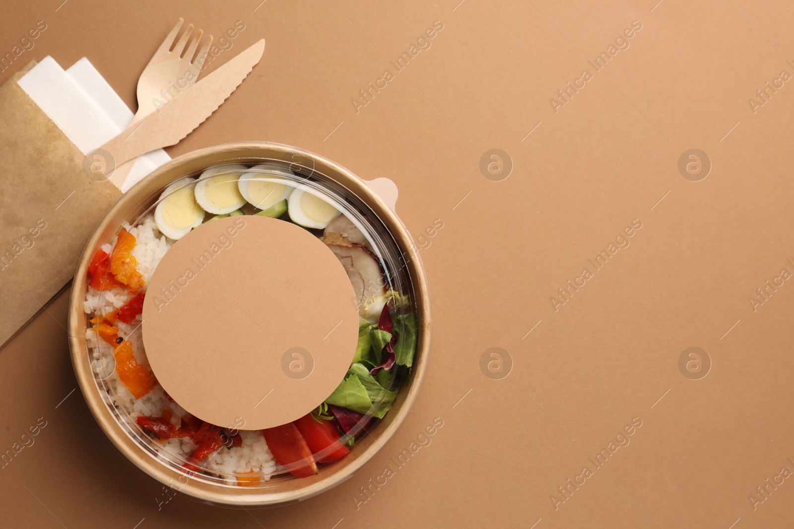 Photo of Tasty food in container with wooden fork and knife on beige background, flat lay. Space for text