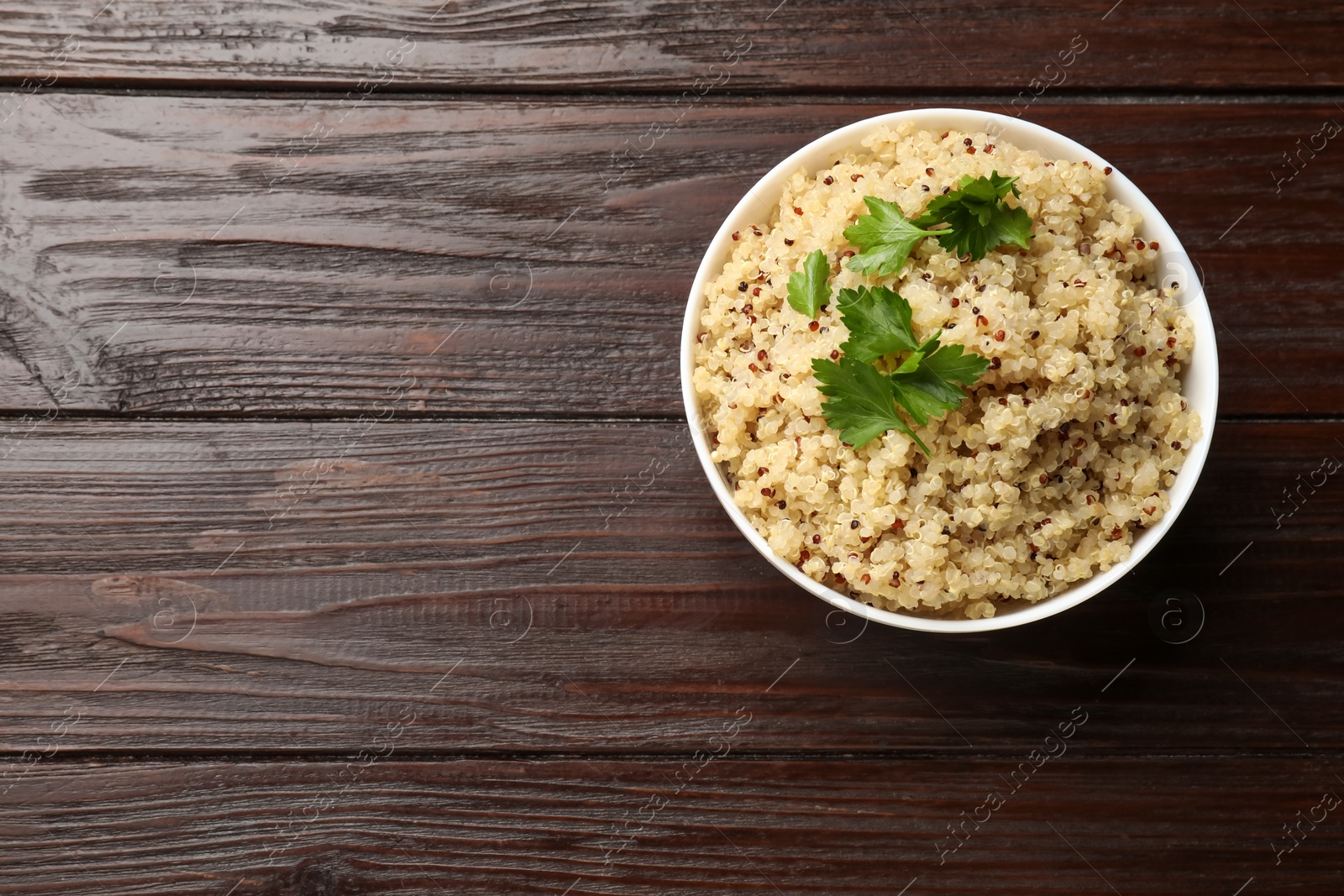 Photo of Tasty quinoa porridge with parsley in bowl on wooden table, top view. Space for text