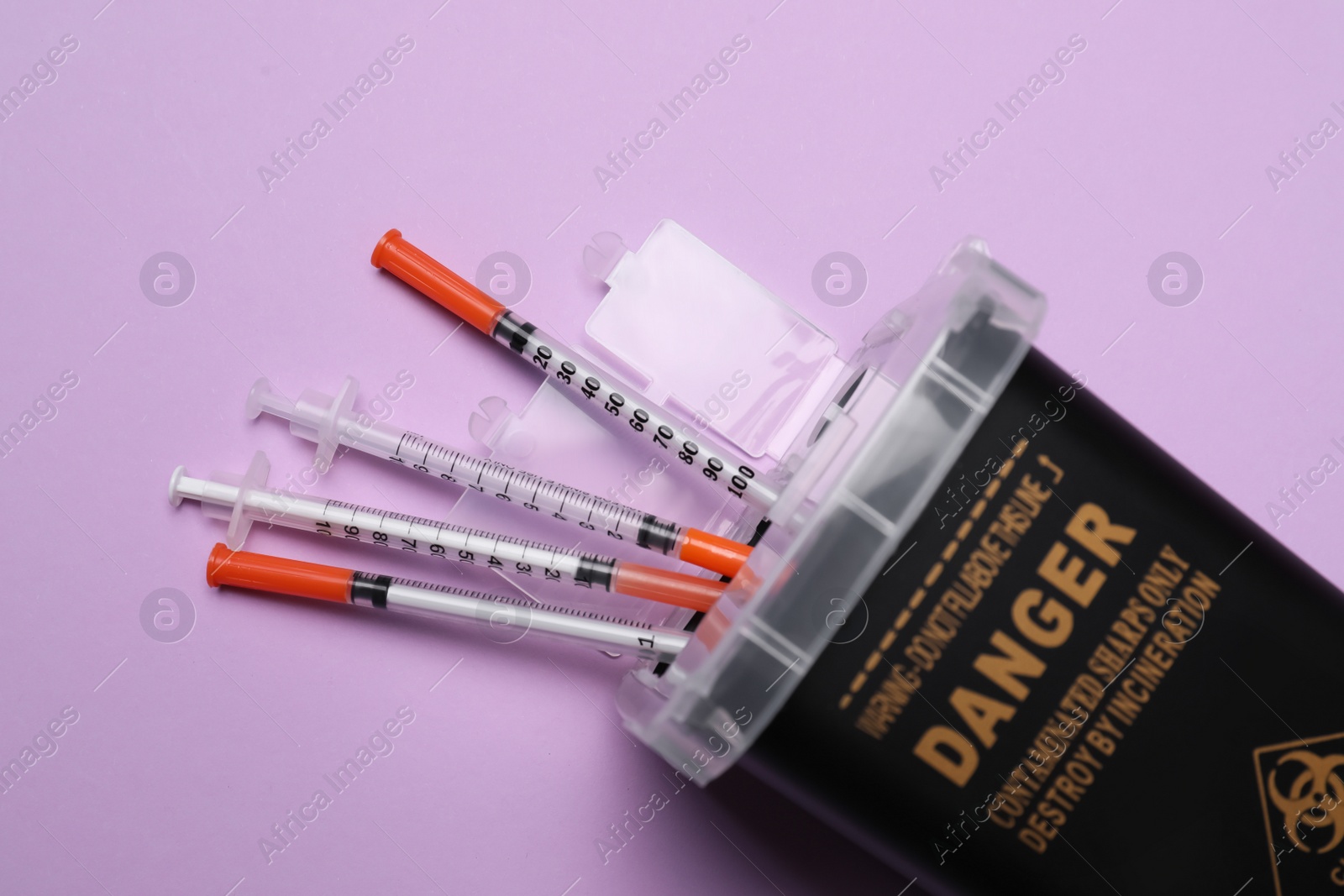 Photo of Disposable syringes and sharps container on violet background, top view