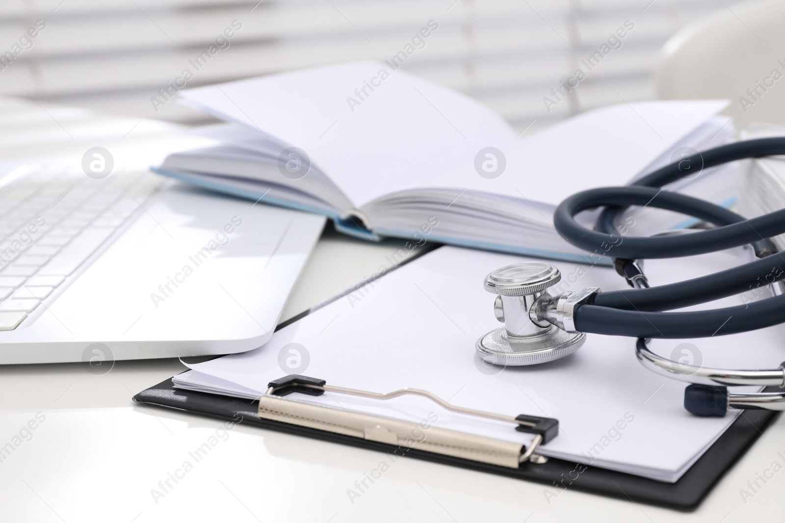 Photo of Book, stethoscope, laptop and clipboard on white table indoors. Medical education