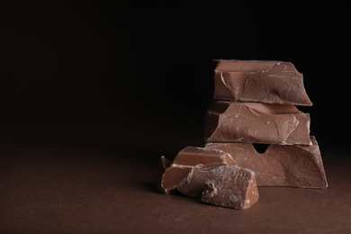 Photo of Pieces of milk chocolate on brown table. Space for text