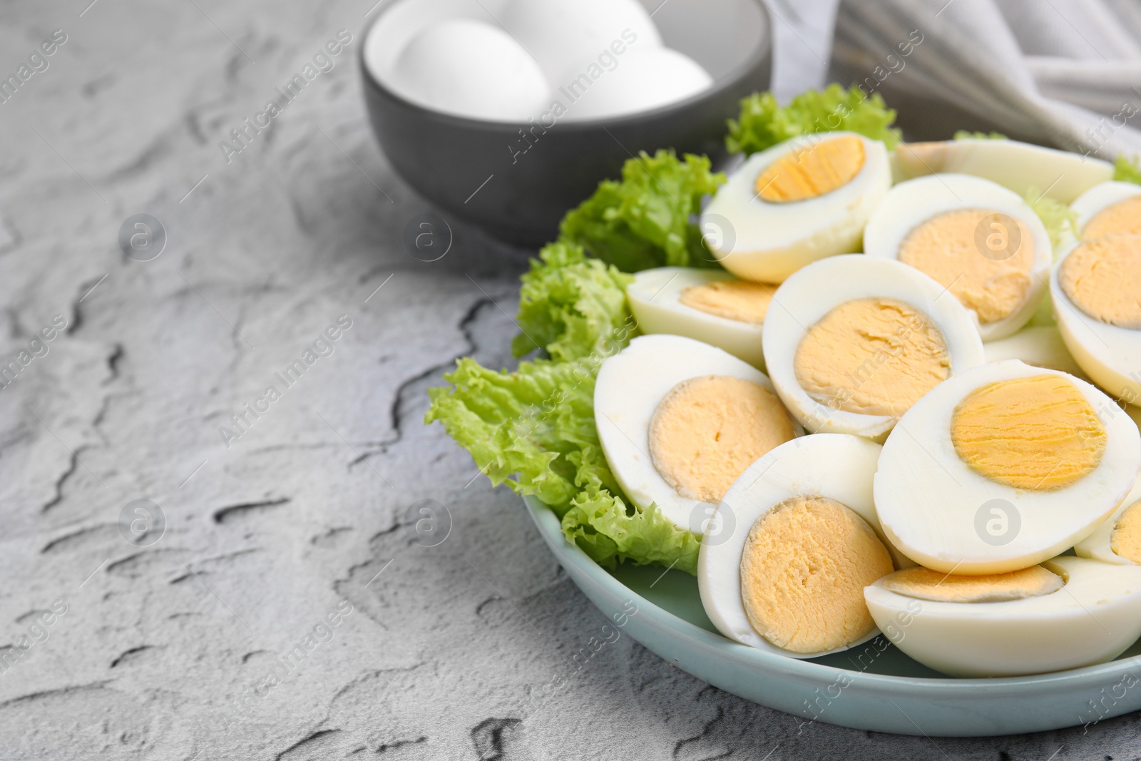 Photo of Fresh hard boiled eggs and lettuce on light grey textured table. Space for text