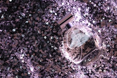 Photo of Luxury perfume in bottle on fabric with violet sequins, top view