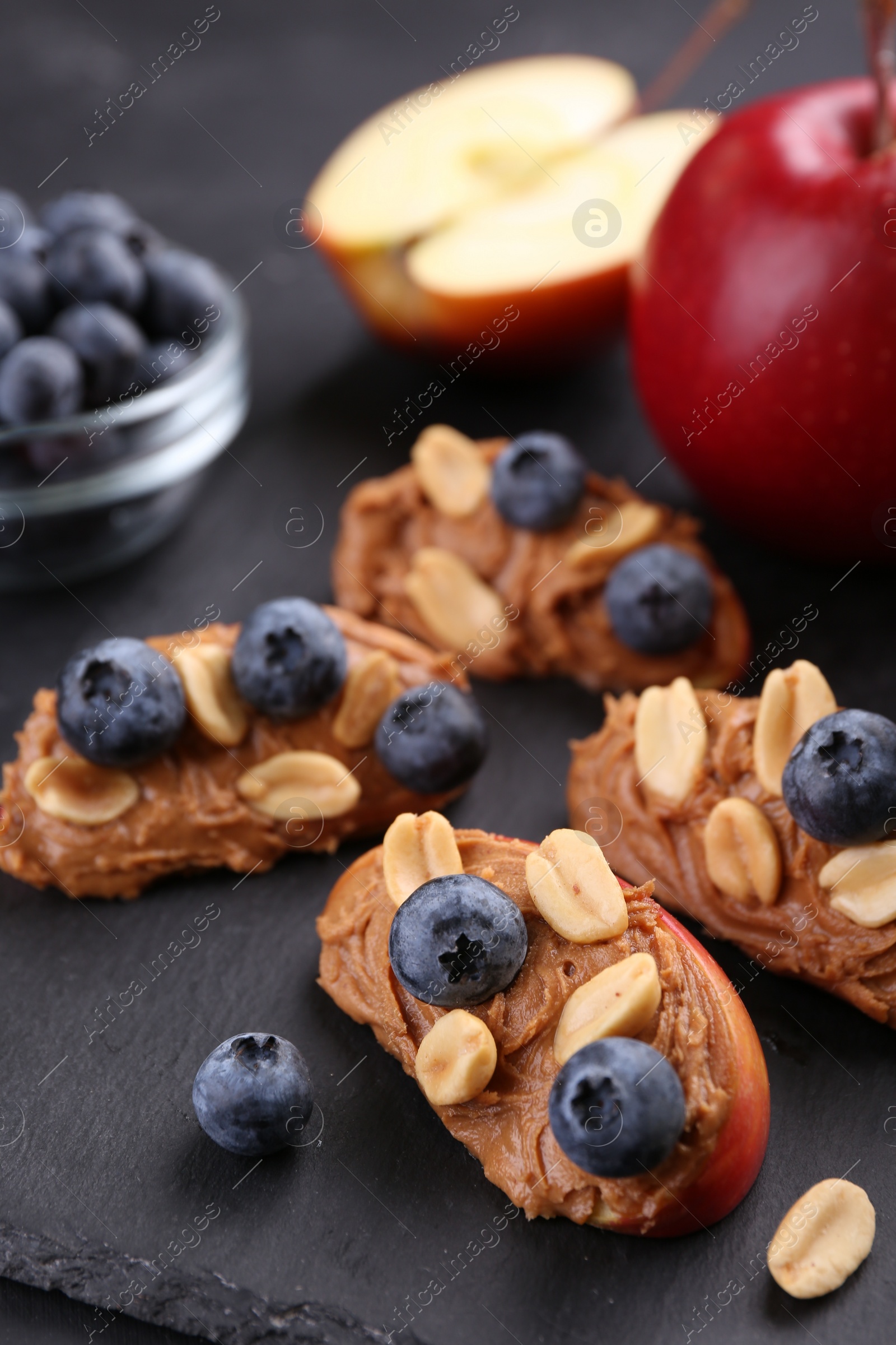 Photo of Fresh apples with peanut butter and blueberries on dark table, closeup