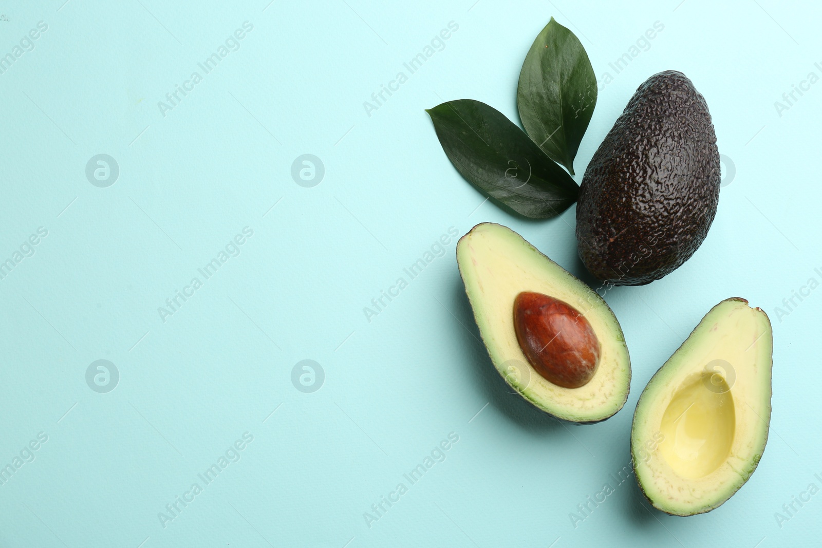 Photo of Whole and cut ripe avocadoes with green leaves on light blue background, flat lay. Space for text