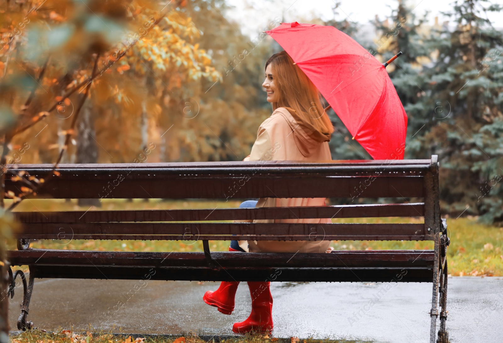 Photo of Woman with umbrella sitting on bench in autumn park. Rainy day