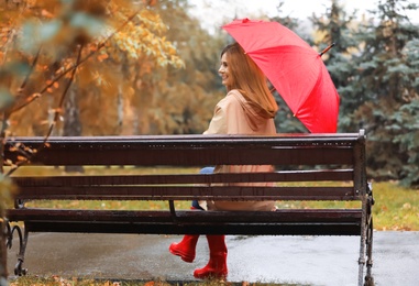 Woman with umbrella sitting on bench in autumn park. Rainy day