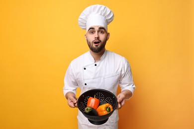 Photo of Surprised chef holding colander with vegetables on yellow background