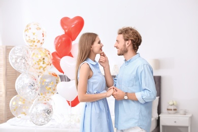 Photo of Young couple with air balloons in bedroom. Celebration of Saint Valentine's Day