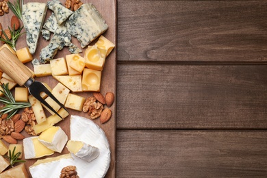 Photo of Cheese plate with rosemary and nuts on wooden table, top view. Space for text