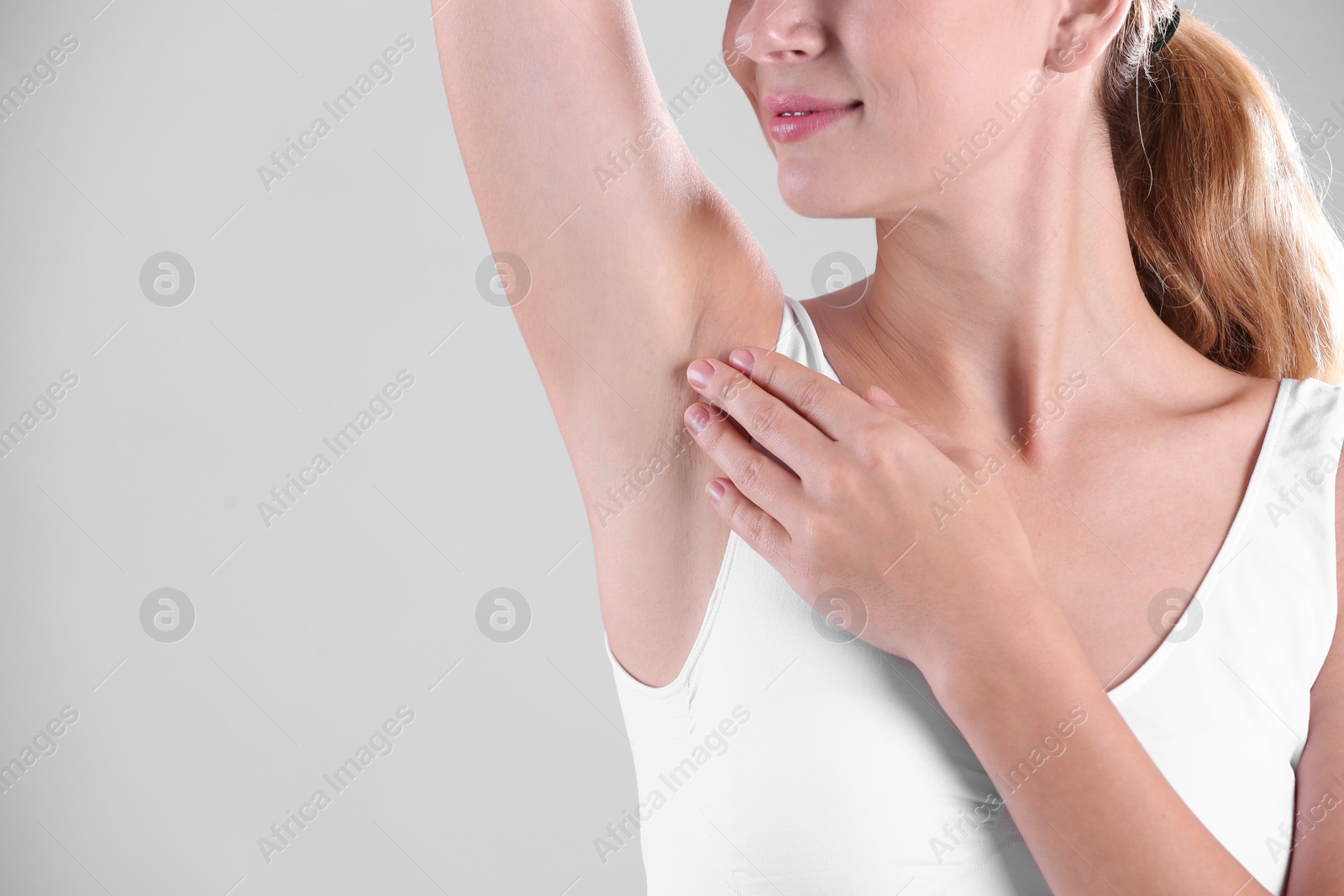 Photo of Young woman showing armpit on grey background, space for text. Using deodorant