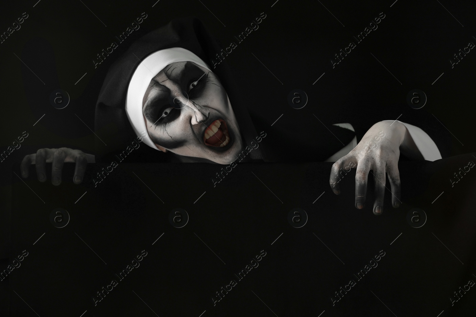 Photo of Portrait of scary devilish nun on black background. Halloween party look