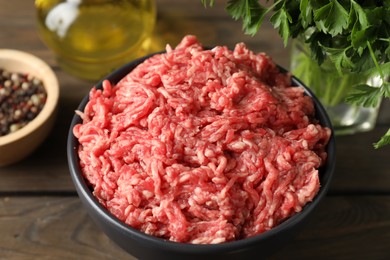 Raw ground meat in bowl and parsley on wooden table, closeup