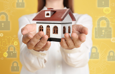 Image of Home security concept. Woman holding house on yellow background, closeup