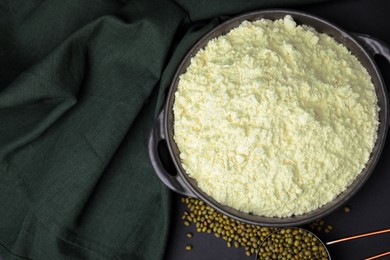 Photo of Pan with flour, mung beans and cloth on black background, flat lay. Space for text