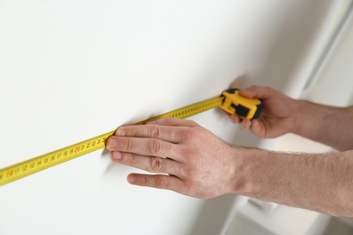 Man measuring white wall indoors, closeup. Construction tool