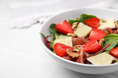 Tasty salad with brie cheese, prosciutto, strawberries and walnuts on white table, closeup. Space for text