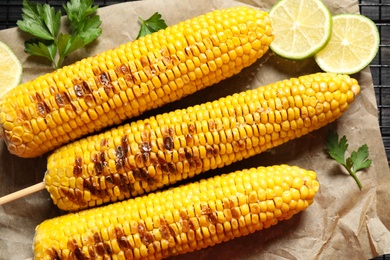 Photo of Tasty grilled corn on parchment, flat lay