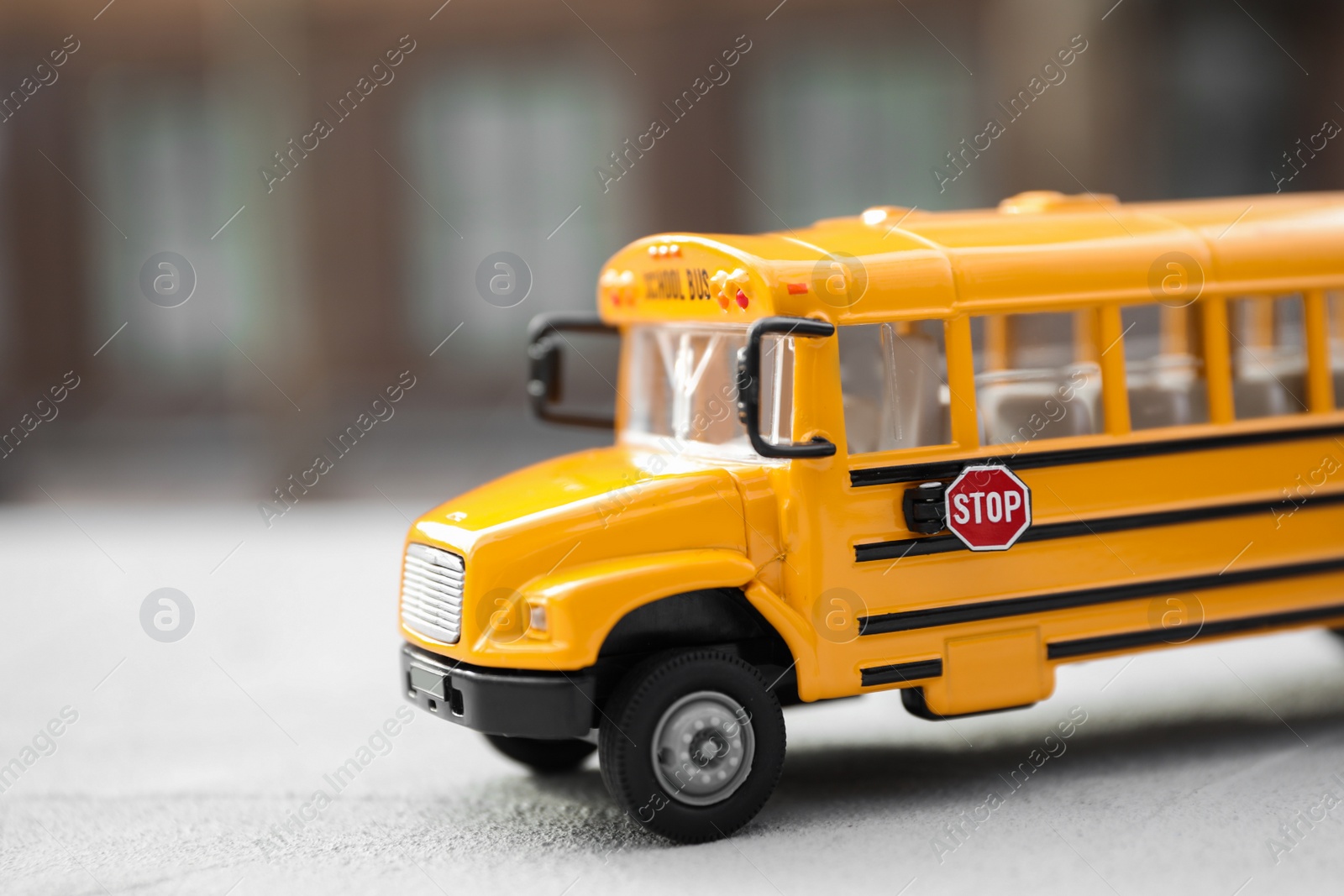 Photo of Yellow toy school bus against blurred 
background, closeup. Transport for students