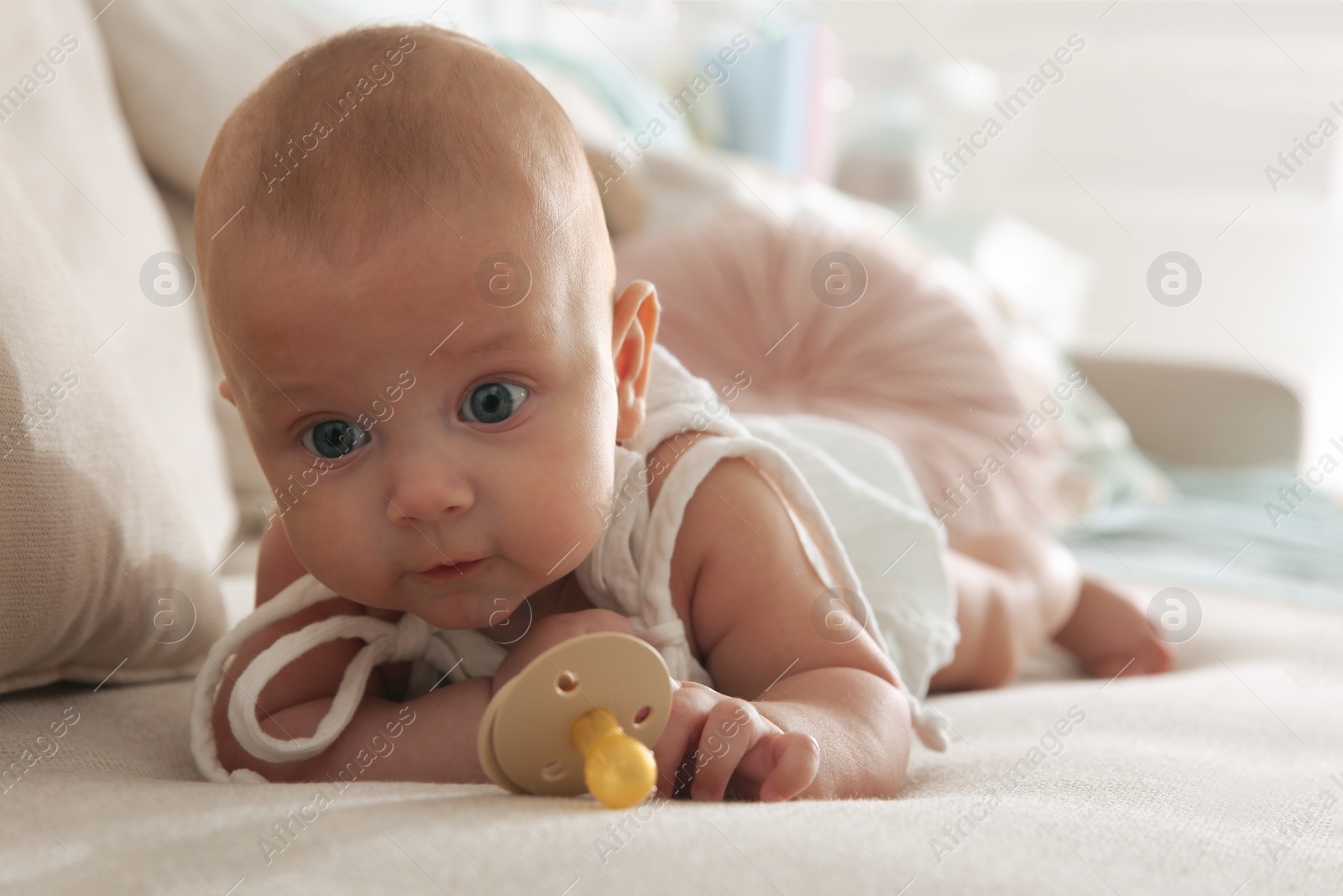 Photo of Cute little baby with pacifier on sofa at home