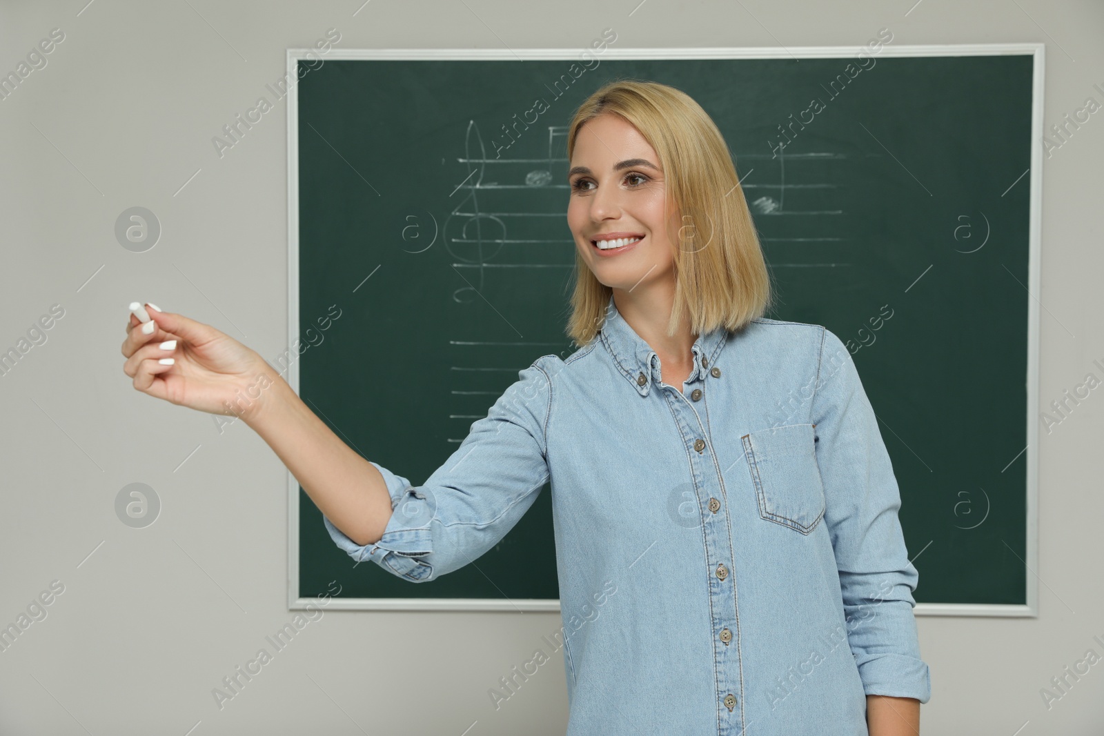 Photo of Teacher near green chalkboard with music notes in classroom