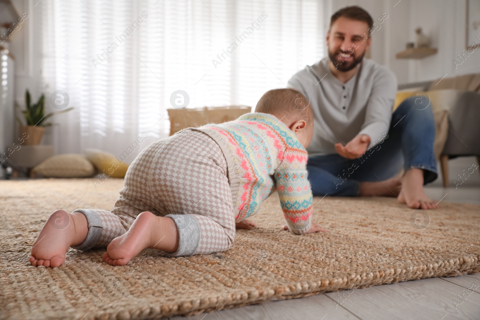 Photo of Happy young father watching his cute baby crawl on floor at home