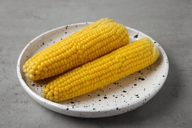 Photo of Plate with tasty boiled corn cobs on light grey table