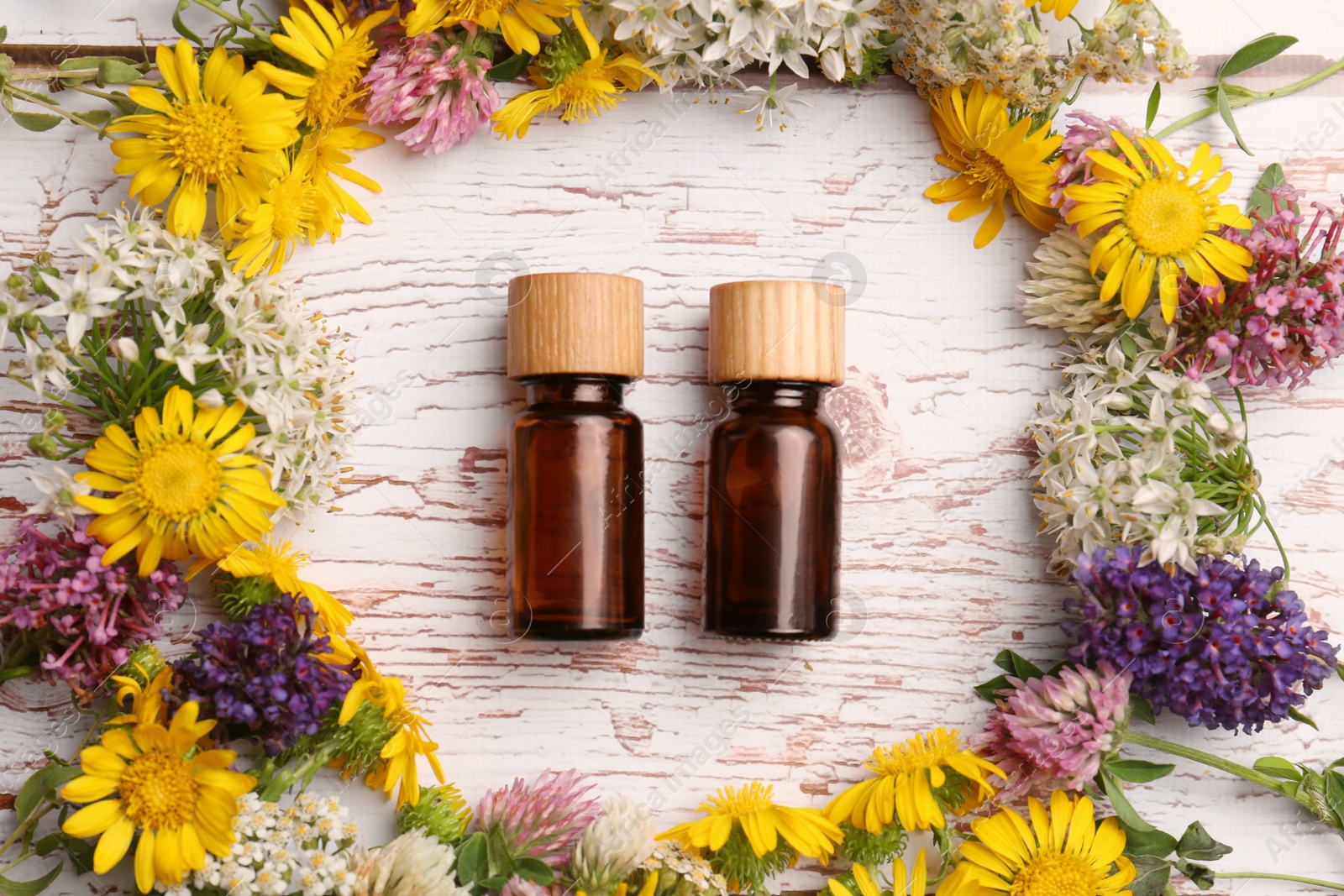 Photo of Flat lay composition with bottles of essential oils surrounded by beautiful flowers on white wooden table