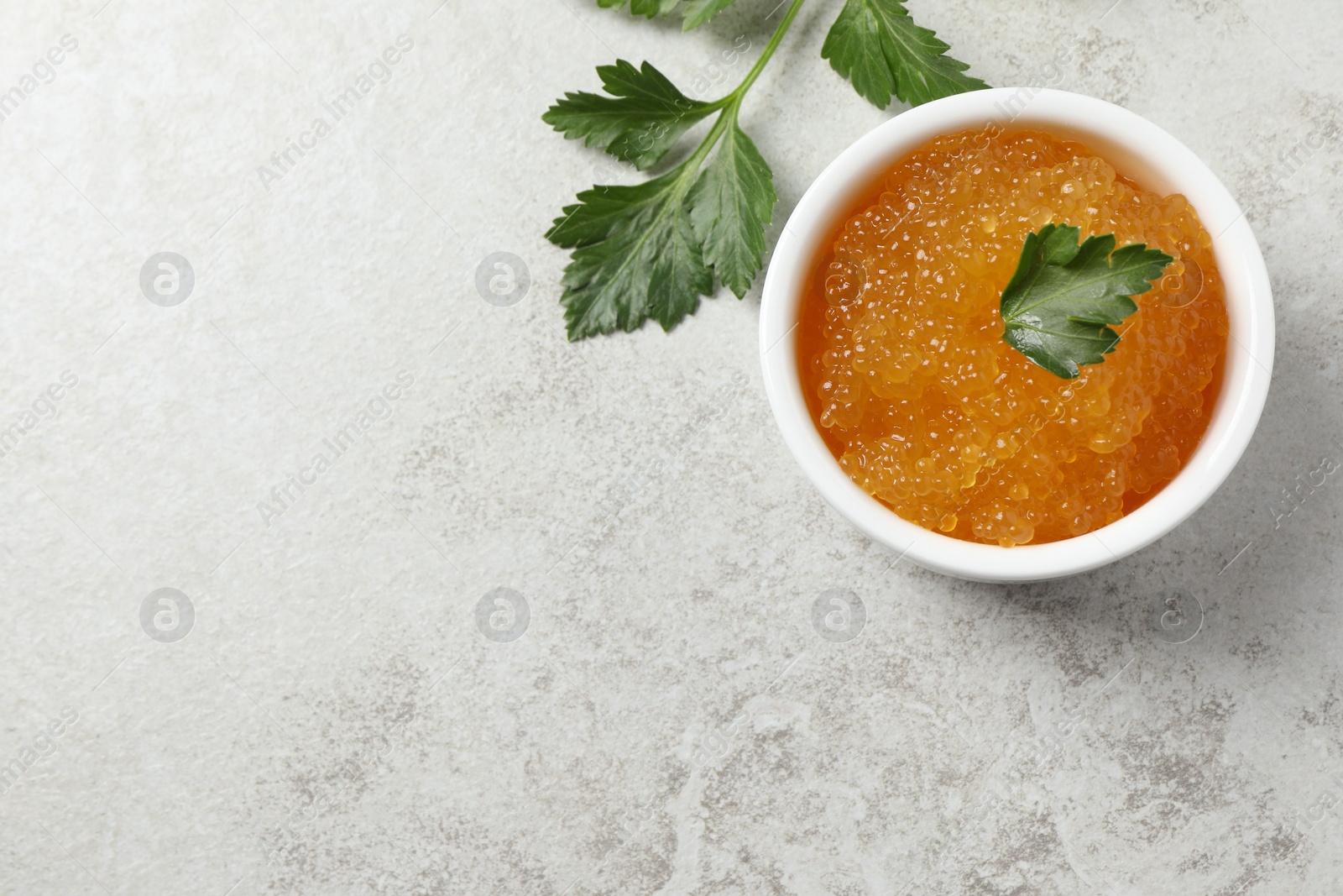 Photo of Fresh pike caviar in bowl and parsley on light grey table, top view. Space for text