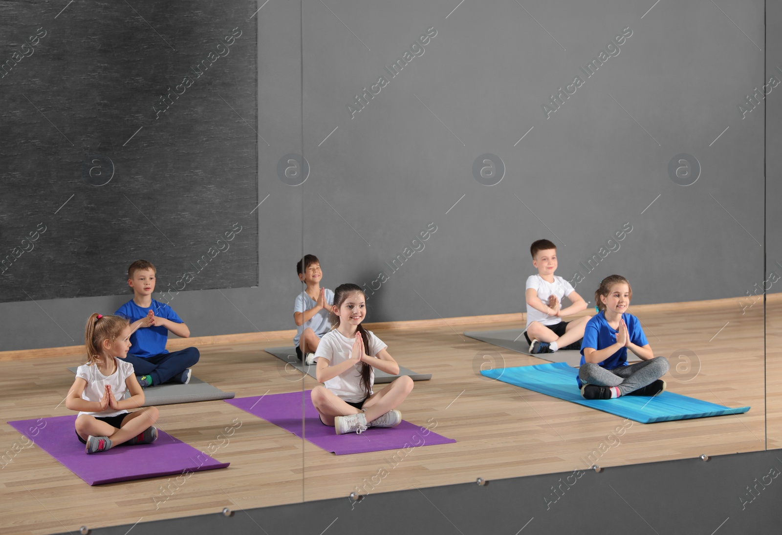 Photo of Cute little children sitting on floor and doing physical exercise in school gym. Healthy lifestyle