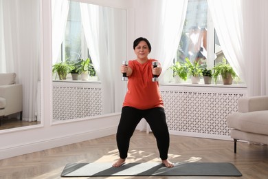 Overweight mature woman doing exercise with dumbbells at home