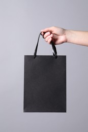 Woman holding paper shopping bag on grey background, closeup