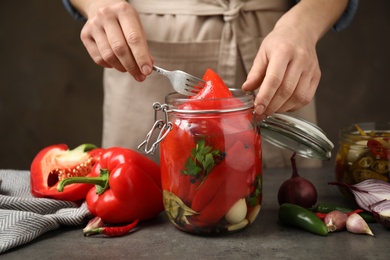 Photo of Woman with jar of pickled peppers at table, closeup
