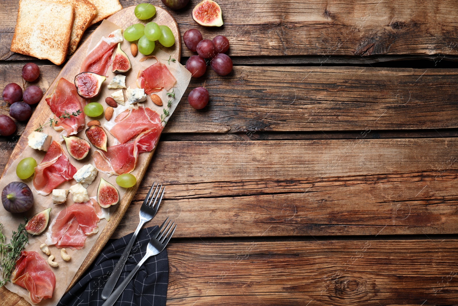 Photo of Ripe figs and prosciutto served on wooden table, flat lay. Space for text