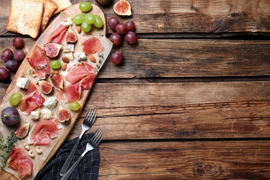 Photo of Ripe figs and prosciutto served on wooden table, flat lay. Space for text