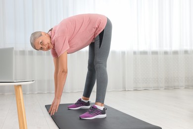 Photo of Senior woman in sportswear stretching on mat at home