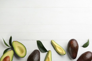 Whole and cut avocados with green leaves on white wooden table, flat lay. Space for text