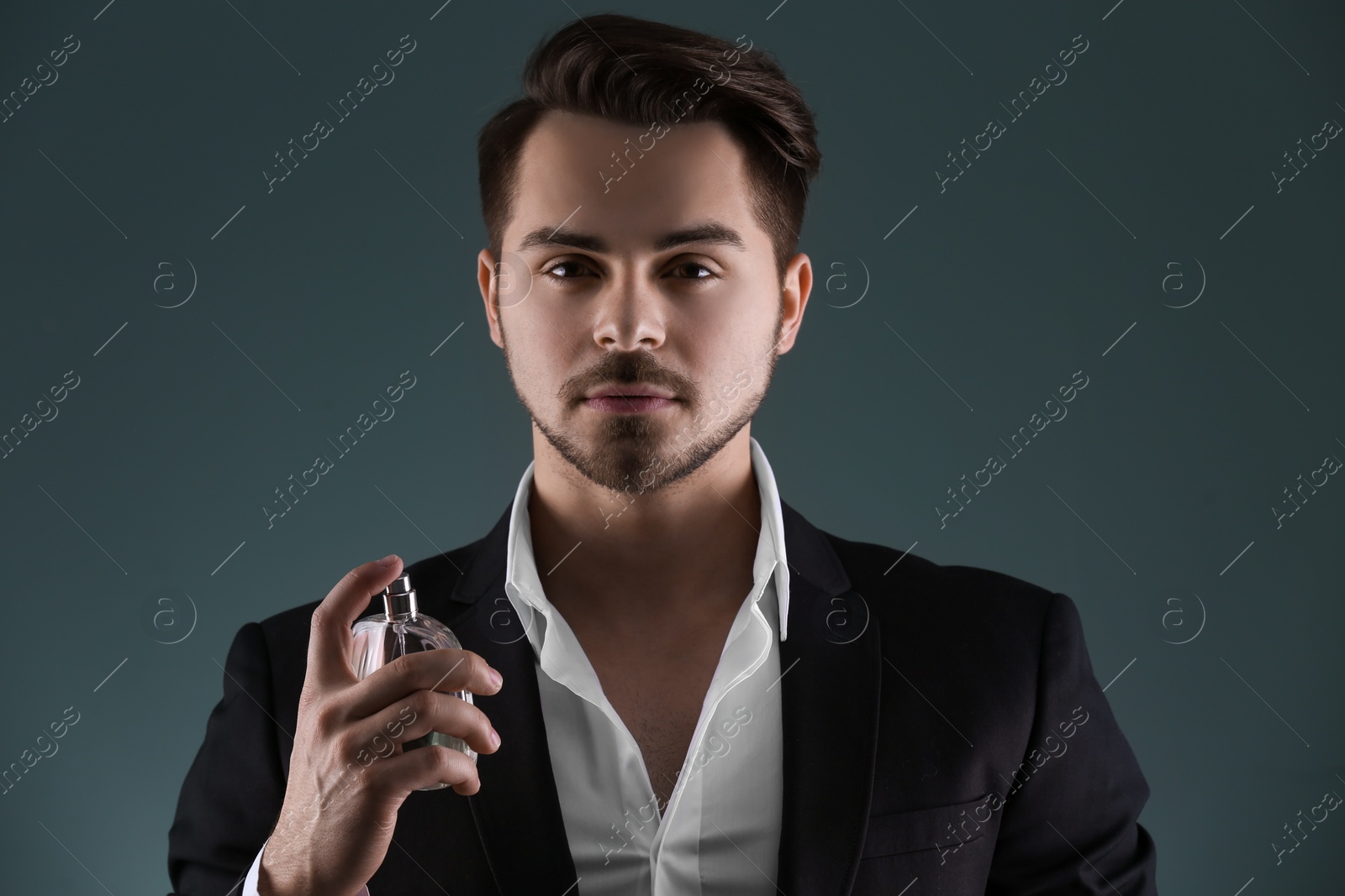 Photo of Handsome man in suit using perfume on dark background