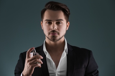 Handsome man in suit using perfume on dark background