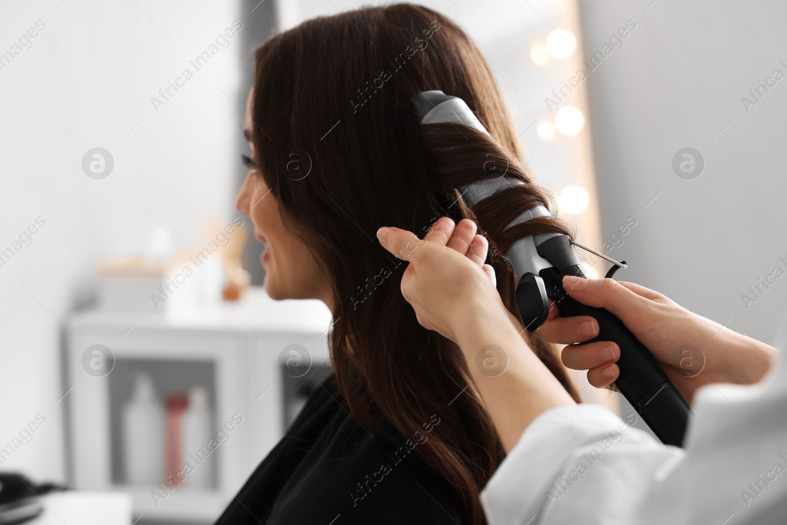 Photo of Hairdresser working with client using curling hair iron in salon, closeup