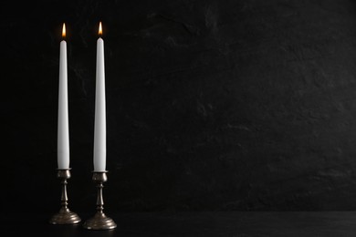 Photo of Elegant candlesticks with burning candles on black table. Space for text