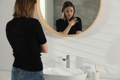 Photo of Sad young woman near mirror in bathroom