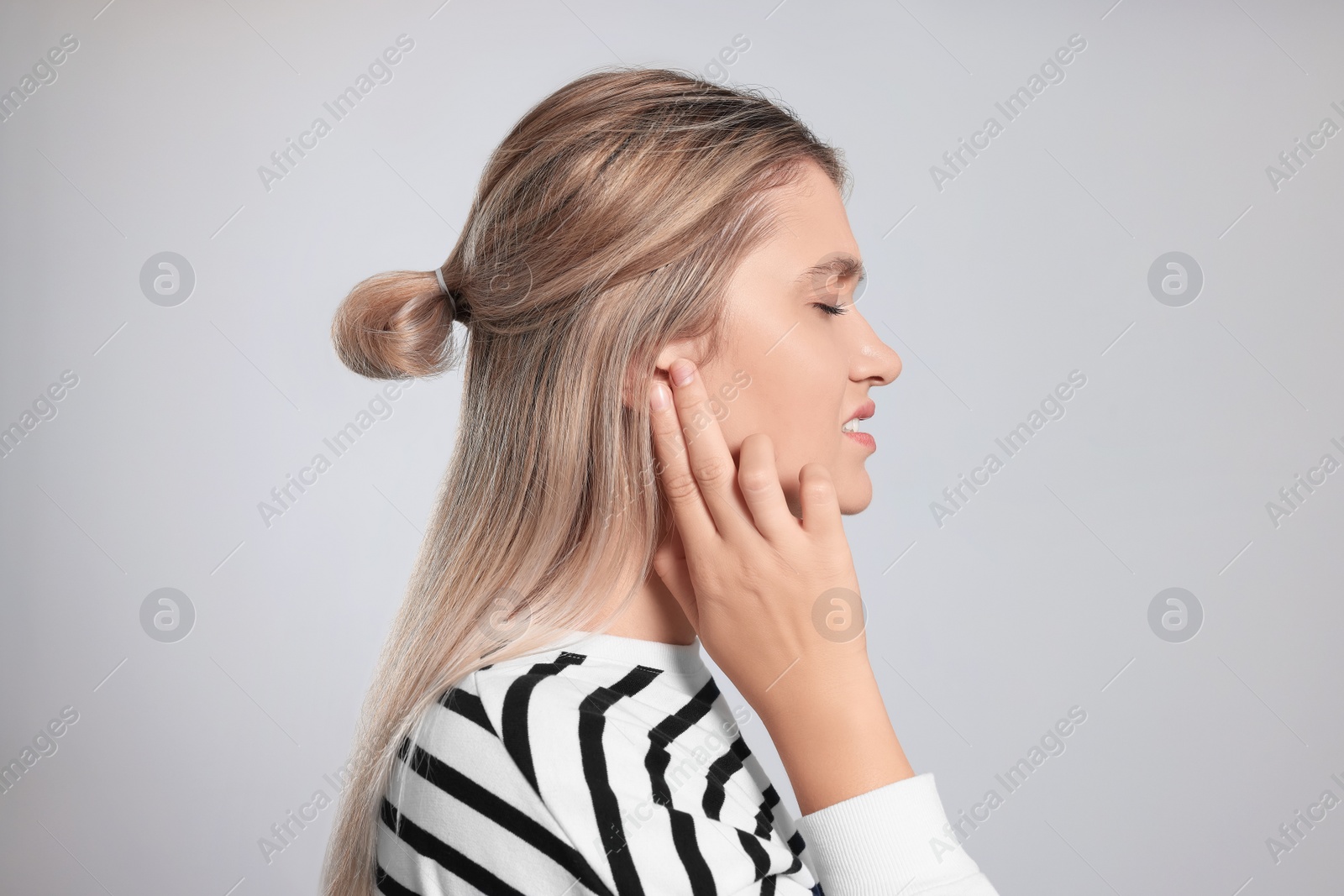 Photo of Young woman suffering from ear pain on light grey background