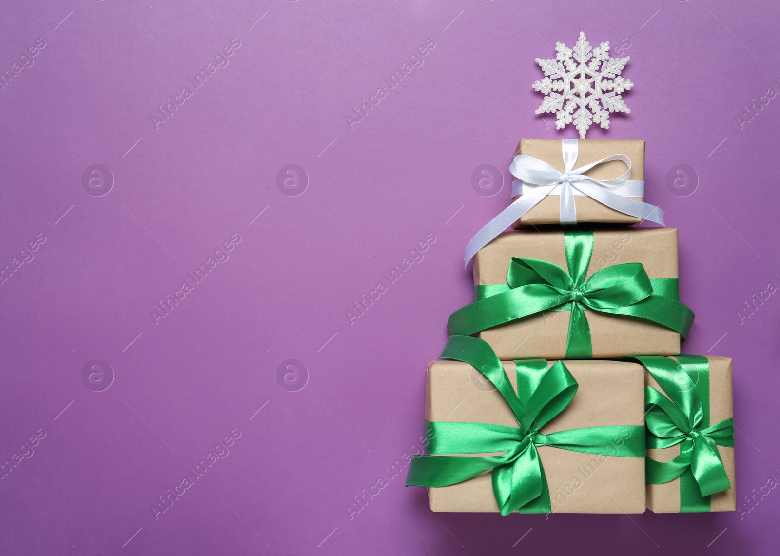 Photo of Christmas tree shape of gift boxes and decorative snowflake on purple background, flat lay. Space for text