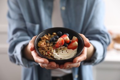 Photo of Woman holding bowl of tasty granola with berries, yogurt and seeds indoors, closeup