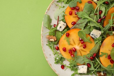 Photo of Tasty salad with persimmon, blue cheese and walnuts served on light green background, top view. Space for text