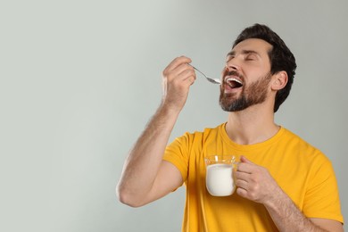 Photo of Handsome man eating delicious yogurt on light grey background. Space for text