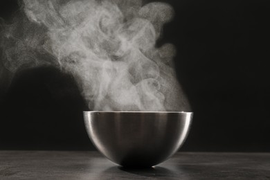 Photo of Steaming metal bowl on grey table against dark background