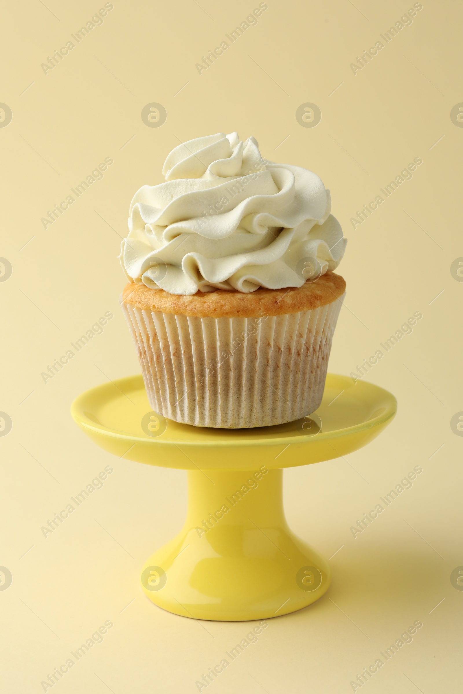 Photo of Tasty vanilla cupcake with cream on pale yellow background