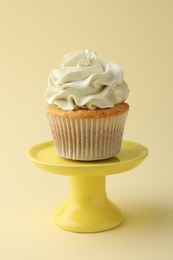 Photo of Tasty vanilla cupcake with cream on pale yellow background